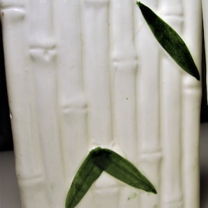 May include: White ceramic planter with a bamboo design and green leaves. The planter is a rectangular shape with rounded corners.