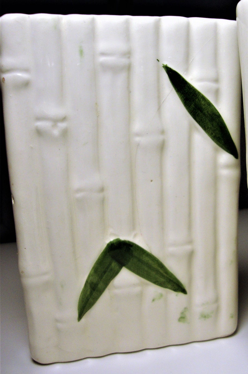 May include: White ceramic planter with a bamboo design and green leaves. The planter is a rectangular shape with rounded corners.