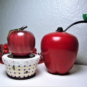 May include: Two red apple-shaped objects. One is a decorative apple with a green leaf on top, the other is a smaller apple on a white and pink checkered base.