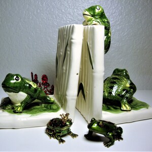 May include: A set of ceramic frog bookends with green and white painted details. The bookends are shaped like frogs sitting on a green base with bamboo stalks. Two smaller jeweled frog figurines are also included.