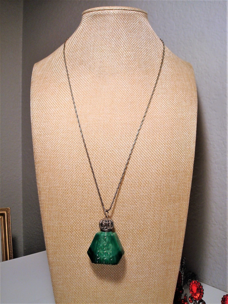 May include: A silver chain necklace with a green glass bottle pendant. The bottle has a detailed silver top and a faceted design.