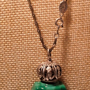 May include: A silver chain necklace with a green glass bottle pendant. The bottle has a silver top with a decorative design and a green glass stopper. The chain has a silver clasp with the text "LVP & Sons" on it.