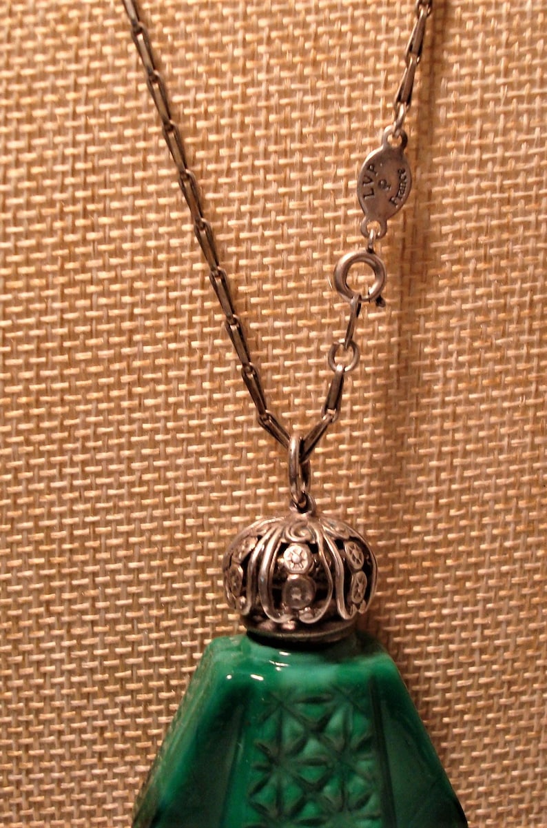 May include: A silver chain necklace with a green glass bottle pendant. The bottle has a silver top with a decorative design and a green glass stopper. The chain has a silver clasp with the text "LVP & Sons" on it.