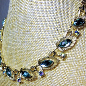May include: A gold tone necklace with a leaf design and teal blue rhinestones.