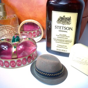 Pu&ograve; includere: Un assortimento di articoli per la cura della persona e decorativi. Include una bottiglia di bagnoschiuma e shampoo Stetson Original, un piccolo cappello fedora grigio con una fascia blu, una saponetta, un flacone di profumo e un portagioie a forma di corona.
