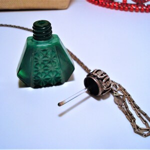 May include: A green glass bottle with a starburst pattern and a silver chain attached to a silver stopper. The bottle is empty and the stopper is removed.