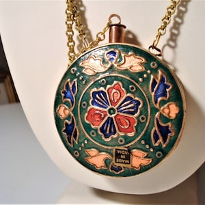 May include: A round, green, gold, and enamel pendant necklace with a floral design. The pendant has a copper top and a chain with a lobster clasp. The pendant has the words "MADE IN INDIA" on the bottom.