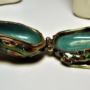May include: A green frog-shaped trinket box with gold accents and red and orange spots. The box is open, revealing a turquoise interior.