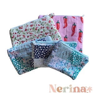 May include: Several handmade quilted zipper pouches with diverse patterns. Designs feature strawberries on white, red chillies on pink, and floral patchwork. The pouches are in shades of blue, green, and white. The brand name "Nerina Allan Handmade" is visible.