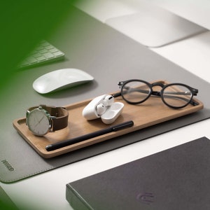 Op de afbeelding: Een houten bureau organizer tray met een horloge, een bril, een pen en een wit etui voor draadloze oordopjes.
