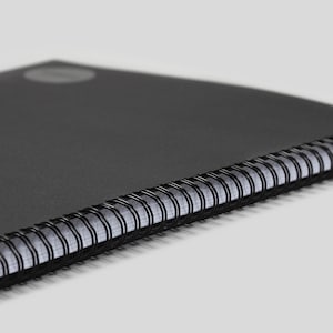 May include: A black spiral bound notebook with a black cover.