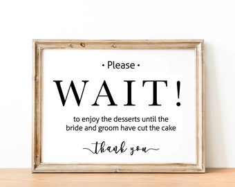 May include: A framed sign with the text "Please WAIT! to enjoy the desserts until the bride and groom have cut the cake. Thank you." in black text on a white background.