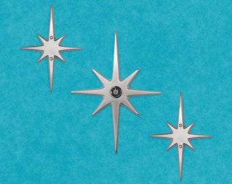 May include: Three silver star-shaped wall decor pieces on a blue background. The stars have a pointed center and six points.