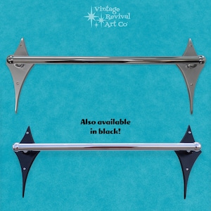 May include: Two silver towel bars with decorative ends in the shape of a diamond. The towel bars are mounted on a blue wall. The text "Also available in black!" is printed below the towel bars.
