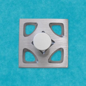 May include: A silver square knob with a white round center. The knob has a geometric design with four cutouts in the shape of a teardrop.