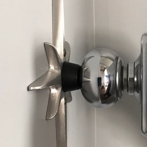 May include: A silver metal wall mount with a star-shaped base and a round ball at the end. The mount is attached to a white wall.