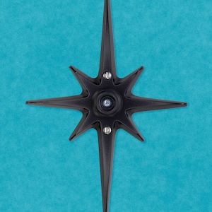 May include: A black metal star-shaped door knocker with a circular center and six points. The knocker is mounted on a blue wall.