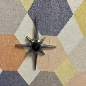 May include: A silver star-shaped door knob with a black center against a background of geometric patterned wallpaper in shades of gray, yellow, and orange.