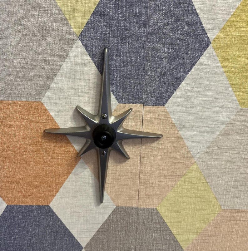 May include: A silver star-shaped door knob with a black center against a background of geometric patterned wallpaper in shades of gray, yellow, and orange.