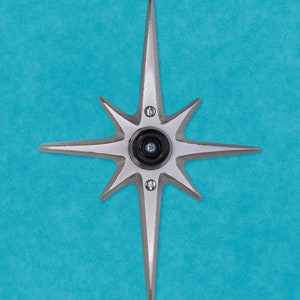 May include: A silver star-shaped door knocker with a black peephole in the center, mounted on a blue wall.