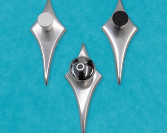 May include: Three diamond-shaped cabinet knobs with different colored centers. The knobs are silver with a black, white, and chrome center.
