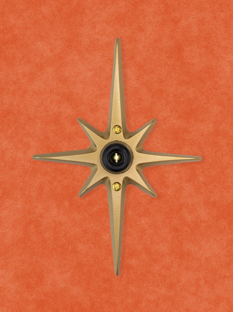 May include: A gold-toned starburst-shaped doorbell button with a black center and a small keyhole.