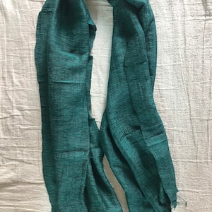May include: A teal green scarf made of a soft, textured fabric. The scarf has a fringed edge.