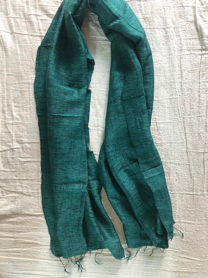 May include: A teal green scarf made of a soft, textured fabric. The scarf has a fringed edge.