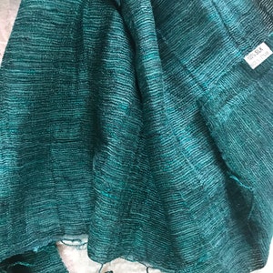 May include: A teal green silk scarf with a textured weave. The scarf has a tag that reads "100% Silk".