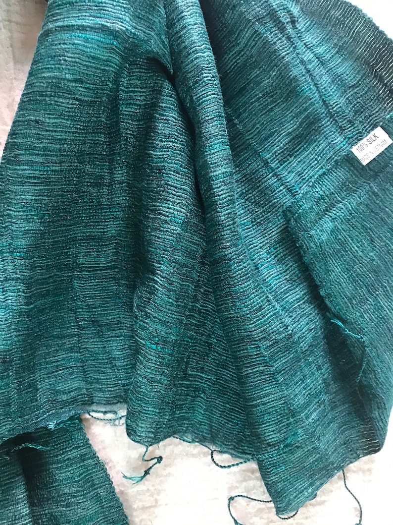 May include: A teal green silk scarf with a textured weave. The scarf has a tag that reads "100% Silk".