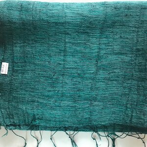 May include: A teal green woven fabric with a textured surface. The fabric has a label that says "100% Silk" and "Made in India".