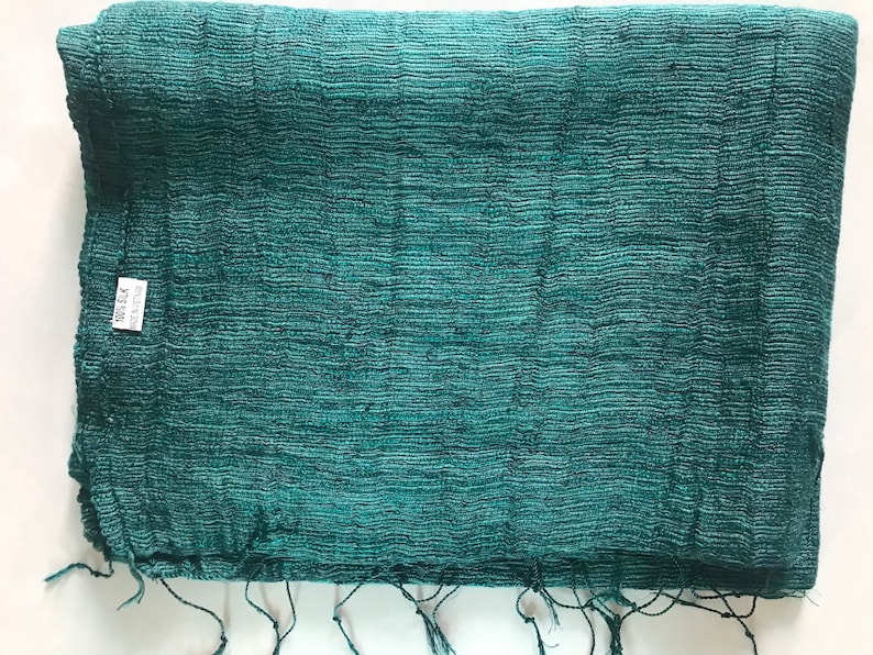 May include: A teal green woven fabric with a textured surface. The fabric has a label that says "100% Silk" and "Made in India".