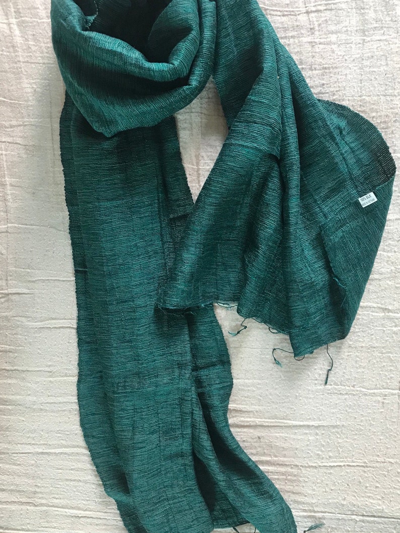 May include: A teal green silk scarf with a fringed edge. The scarf is made of a soft, lightweight fabric and has a subtle sheen.