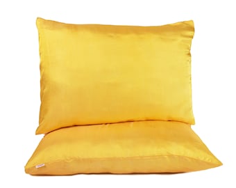 May include: Two golden-yellow satin pillowcases stacked on top of each other. The pillowcases have a smooth, lustrous texture and a rectangular shape. The pillows are a bright, solid color, and are set against a white background.