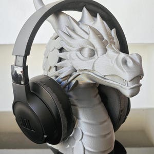 May include: A gray dragon sculpture with black JBL headphones. The dragon has detailed scales and a textured surface. The headphones are over-ear style, with the JBL logo visible on the earcups. The sculpture is a unique decorative item.