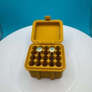 May include: A yellow plastic storage case with a hinged lid, containing multiple compartments for storing batteries. Two batteries are visible in the case.