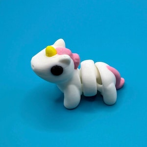 May include: A white unicorn toy with a pink mane and tail, a yellow horn, and black eyes. The toy is made of flexible plastic and is segmented, allowing it to bend and pose.
