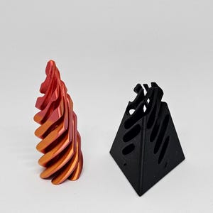 May include: Two abstract sculptures. One is a spiraling, vertical form with a gradient of red to orange hues. The other is a black, geometric pyramid shape with cut-out sections, creating an open, airy design.