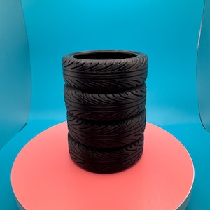 May include: A stack of four black tire-shaped pencil holders on a pink circular surface. The surface is on a blue background.