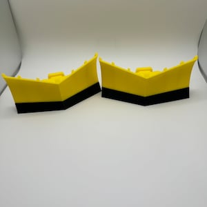 May include: Two yellow plastic snow plow blades with black bases. The blades are angled and have a rounded front edge.