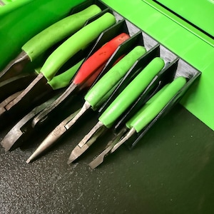 May include: A collection of pliers with green and red handles, neatly organized in a black tray within a green toolbox drawer. The pliers are made of metal and have various tip shapes for different tasks.