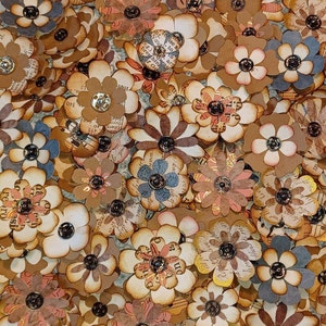 May include: A collection of paper flowers in various shades of brown, beige, and gray. The flowers have a vintage look and are decorated with printed text and metallic accents.