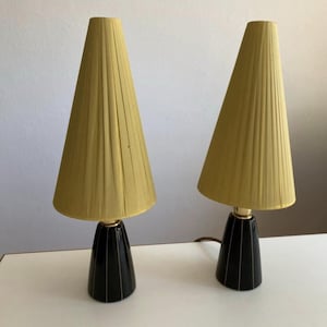Könnte beinhalten: Zwei vintage Tischlampen mit schwarzen und goldenen Sockeln und gefalteten gelben Lampenschirmen.