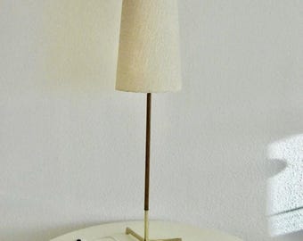 May include: A mid-century floor lamp featuring a cream-coloured, tapered shade. It has a dark brown pole, a brass base, and a white cord with a switch. The lamp is on a white table, a classic design.