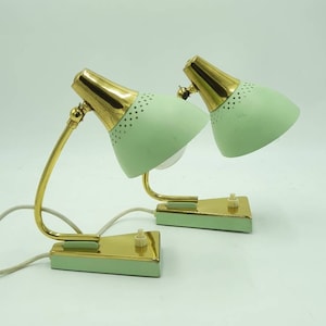 Könnte beinhalten: Zwei Vintage-Schreibtischlampen. Jede Lampe hat einen mintgrünen Schirm mit goldfarbenem Oberteil und passendem Sockel. Die Lampen haben einen gebogenen, goldfarbenen Arm und ein weißes Kabel. Die Lampen stehen auf weißem Hintergrund.