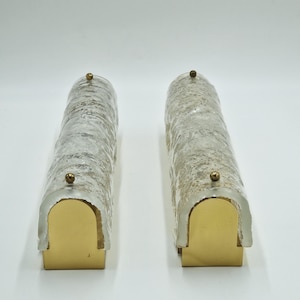 Puede incluir: Dos apliques de pared vintage. Cada aplique presenta una pantalla cilíndrica de vidrio texturizado sobre una base de metal dorado. Un pequeño detalle redondo de color dorado se encuentra en la parte superior de cada aplique. Sobre fondo blanco.