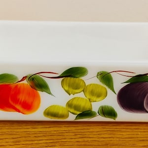 May include: White rectangular baking dish with a painted design of fruit and leaves. The fruit includes peaches, plums, and green grapes.