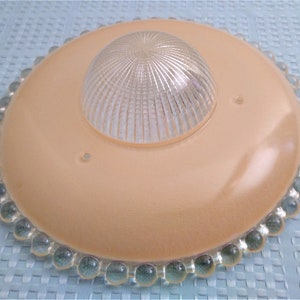 Pu&ograve; includere: Un'antica plafoniera con una base circolare color pesca e una cupola di vetro trasparente e scanalato al centro. Il bordo &egrave; decorato con perline di vetro trasparenti e arrotondate. Progettata per l'illuminazione a soffitto.