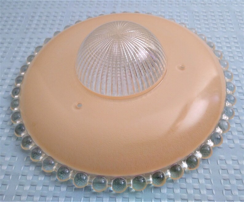 Pu&ograve; includere: Un'antica plafoniera con una base circolare color pesca e una cupola di vetro trasparente e scanalato al centro. Il bordo &egrave; decorato con perline di vetro trasparenti e arrotondate. Progettata per l'illuminazione a soffitto.
