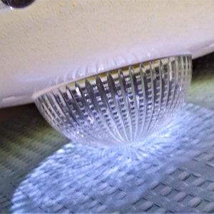 Pu&ograve; includere: Una ciotola di vetro trasparente e scanalato con un bordo arrotondato bianco sporco. La ciotola &egrave; parzialmente illuminata, proiettando un'ombra sulla superficie strutturata sottostante. Il design presenta superfici lisce e strutturate.